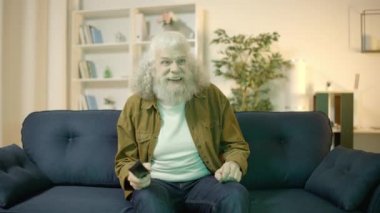 Mutlu yaşlı adam futbol maçı izliyor, el sallıyor, takım zaferini kutluyor.