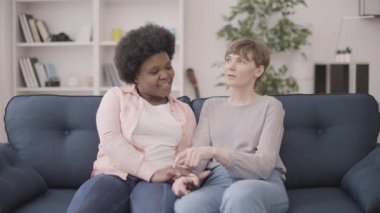 Lezbiyen çift kanepede el ele tutuşuyorlar, evde romantik bir buluşmanın tadını çıkarıyorlar.