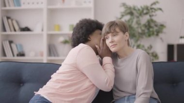 Kafası karışmış Afrikalı bir kadın Kafkasyalı bir bayan arkadaşına sırrını fısıldıyor.