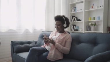 Rahat Afrikalı bir kadın kulaklıkla favori müzikten hoşlanıyor, mobil uygulama kullanıyor.