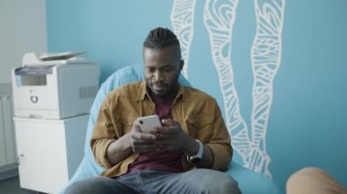 Akıllı telefon uygulaması kullanan genç bir Afrikalı açık uzay ofisinde oturuyor.