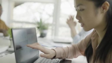 Asyalı bayan pazarlamacı meslektaşlarıyla konuşuyor, ofiste iş planını tartışıyor.