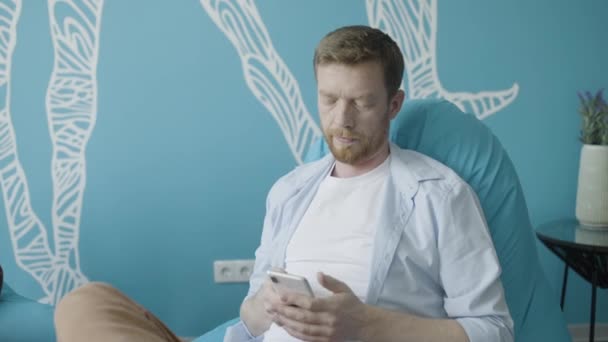 オープンスペースオフィス ビジネスアプリでスマートフォンを使用して赤髪の男性フリーランサー — ストック動画