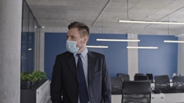空のオフィスを見て顔のマスクで悲しいビジネスマン 会社へのパンデミックの影響 — ストック動画