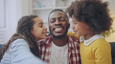 Mutlu küçük kız kardeşler sevgi dolu babaların yanaklarını öpüyor, aile kucaklaşıyor ve gülümsüyor.