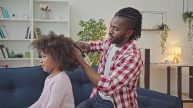 Afrikalı baba, küçük kızın kıvırcık saçlarını tarıyor, ebeveynlik yapıyor.