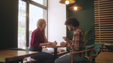 Karışık ırktan erkek ve kadın arkadaşlar birlikte kahve içip kafede sohbet ediyorlar.