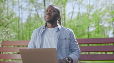 Yeşil Park 'ta dizüstü bilgisayarda çalışan genç bir erkek bankta, küçük bir mola veriyor.