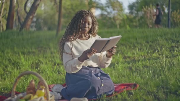 公園で巻き毛読書本を持つ美しいアフリカの女性 レジャー活動 — ストック動画