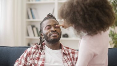 Gülen babaya pembe göz farı süren küçük bir kız, aile eğleniyor, şaka yapıyor.