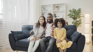 Şirin Afro-Amerikan kızları ve babaları kanepede oturup televizyon seyrediyorlar.