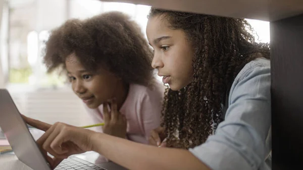 Young sisters with natural black hair watching online lesson, distance learning