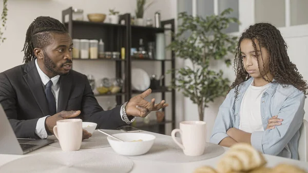 Sad african girl refusing to eat breakfast, dad trying to talk with daughter