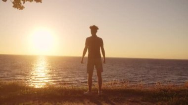 Güçlü adam ağır çekimde kollarını kaldırıyor, sabahın erken saatlerinde denizin tadını çıkarıyor, gücü hissediyor.