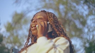 Afro saçlı güzel bir kadın telefonda konuşuyor ve parkta yürürken tablet tutuyor.