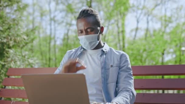 Молодий Чорний Чоловік Масці Має Відеодзвінок Зеленому Парку Працює Відкритому — стокове відео