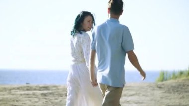 Mutlu erkek ve kadın el ele tutuşup kumsalda yürüyor, romantik bir randevu.