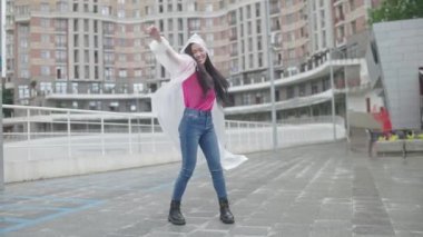 Yağmurluklu mutlu Asyalı kadın sokakta zıplıyor ve dans ediyor, özgürlük.