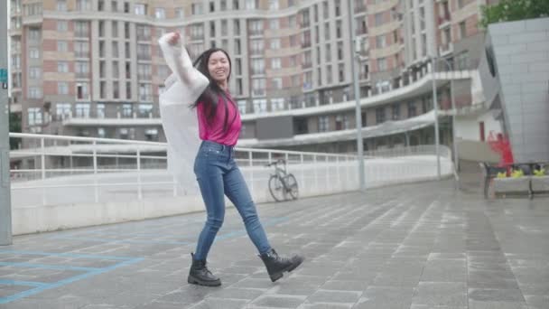 路上で踊る白いレインコートの美しいアジアの女性学生 お祝い — ストック動画