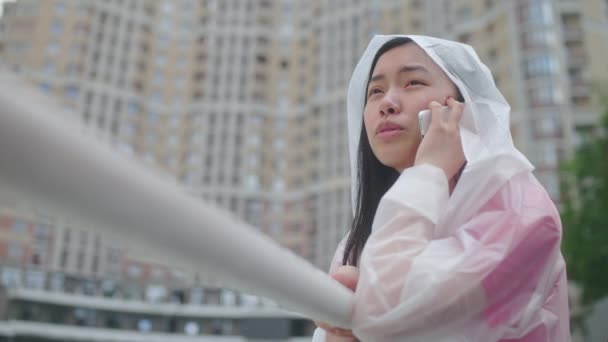 Molesto Mujer Asiática Impermeable Hablando Por Teléfono Ciudad Lluviosa Llamando — Vídeo de stock
