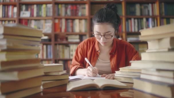 本からノートを書く勤勉なアジアの学生 図書館で働く作家 — ストック動画