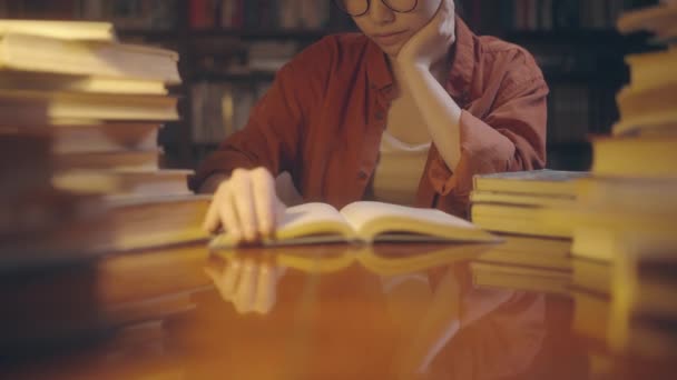 夜に図書館で文学を学ぶ眼鏡のアジアの女性 本を読む — ストック動画