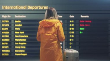 Bavullu genç bayan havalimanı kalkış panosuna bakıyor.