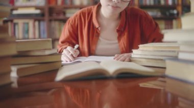 Gözlüklü kız öğrenci not alıyor, üniversite kütüphanesinde kitap okuyor.