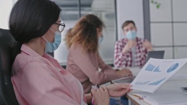 Koruyucu maskeli şirket yöneticileri ofiste raporları tartışıyor, covid-19.