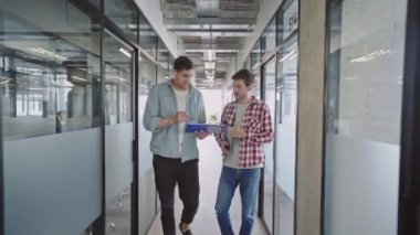 Erkek tasarımcılar iş tartışıyor, ofis koridorunda yürüyor, reklam ajansı