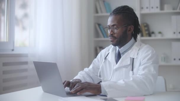 Черный Мужчина Терапевт Работающий Ноутбуке Клинике Онлайн Консультация Здравоохранения — стоковое видео