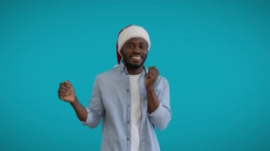 Noel şapkalı neşeli genç adam mavi arka planda dans ediyor, yeni yıl indirimi