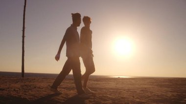 Kumsalda el ele tutuşan ve deniz kenarında yürüyen iki adamın aşk ilişkisi.