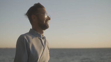 İyimser genç adam güneşin doğuşuna bakıyor, yüzünde gülümseme, başarı için motive olmuş.