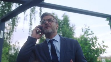 Takım elbiseli kızgın patron dışarıda yürürken telefonda konuşuyor, işte sorunlar var.