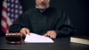 Erkek yargıç gazete okuyor ve tokmağı üç kez vuruyor.