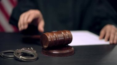 Erkek yargıç son karar için tokmağı vurdu, kelepçeler mahkeme masasında yatıyor.