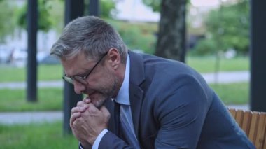 Sinirli iş adamı parkta bankta oturuyor, zor kararlar veriyor, sorunlar yaşıyor.