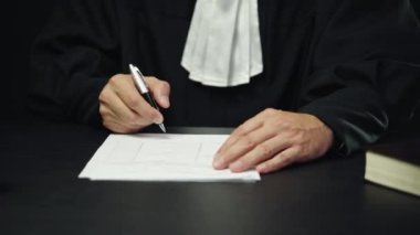 Siyah cüppeli erkek yargıç evrakları imzaladı, dava kapandı, adalet yerini buldu.