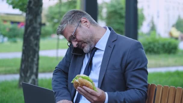 Többfunkciós Férfi Szabadúszó Telefonál Laptopozik Hamburgert Eszik — Stock videók