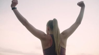 At kuyruklu atletik bir kadın sabah gökyüzüne ve güneşe el kaldırıyor.