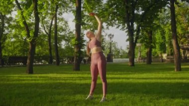 Genç bir kadın egzersiz yapıyor, parkta ısınıyor, sağlıklı bir hayat sürüyor.