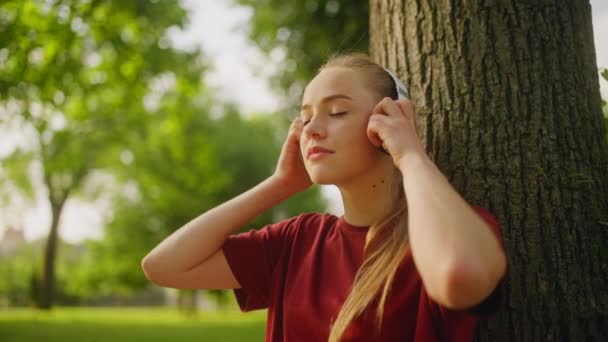 Mladá Šťastná Žena Nasazuje Sluchátka Užívá Hudbu Sedí Pod Stromem — Stock video