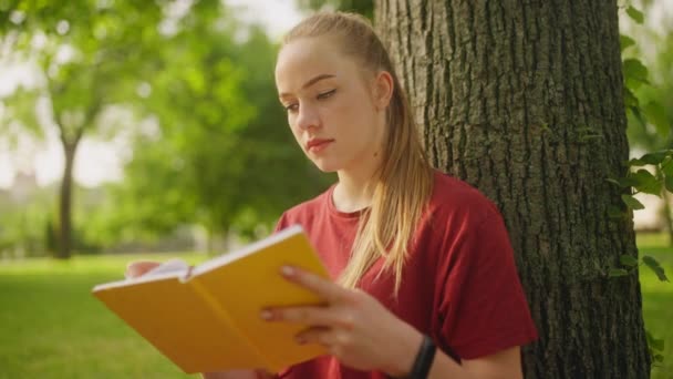Genç Sarışın Kadın Ilginç Bir Kitap Okuyor Parktaki Ağacın Altında — Stok video