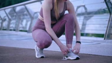 Spordaki kadın koşucu ayakkabı bağcıklarını spor ayakkabısına bağlayıp antrenmana devam ediyor.