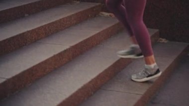 Spor elbiseli atletik bir kadın ve merdivenlerden çıkan rahat ayakkabılar.