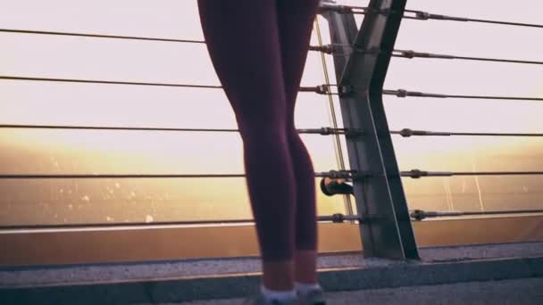 橋の上で美しい日の出と街並みを楽しむスポーツウェアのスリム女性 — ストック動画