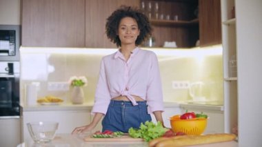 Mutfakta kameraya bakan gülümseyen siyah kadın, vejetaryen diyeti, yemek pişirme tavsiyeleri.