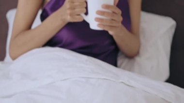 Mutlu genç bayan sabah kahve kokusunun tadını çıkarıyor, yatakta oturuyor, dinleniyor.