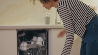 Bulaşık makinesinden temiz bardak alan tatmin olmuş bir kadın. Etkili temizlik, hijyenik temizlik.